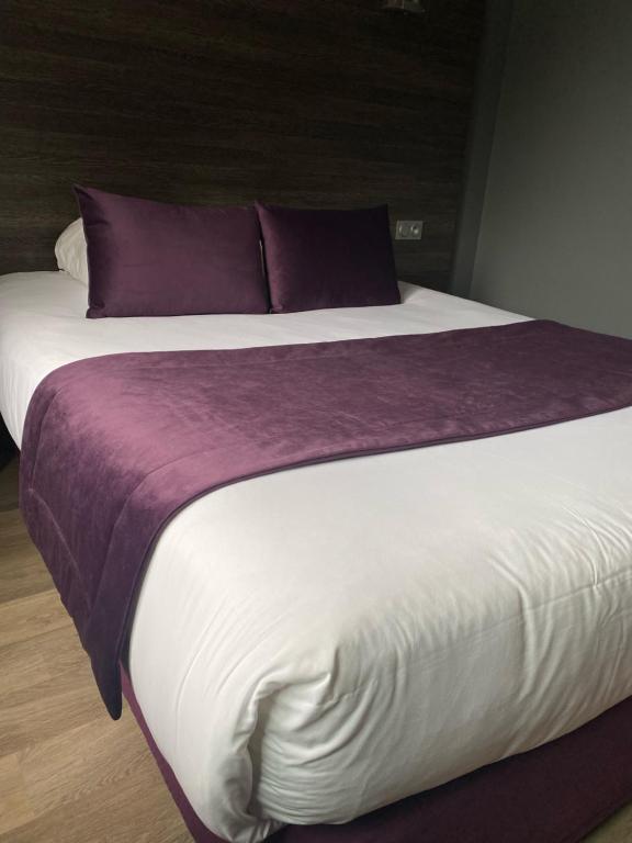 een groot bed met paarse en witte lakens en kussens bij Hotel Restaurant Vesontio in Besançon