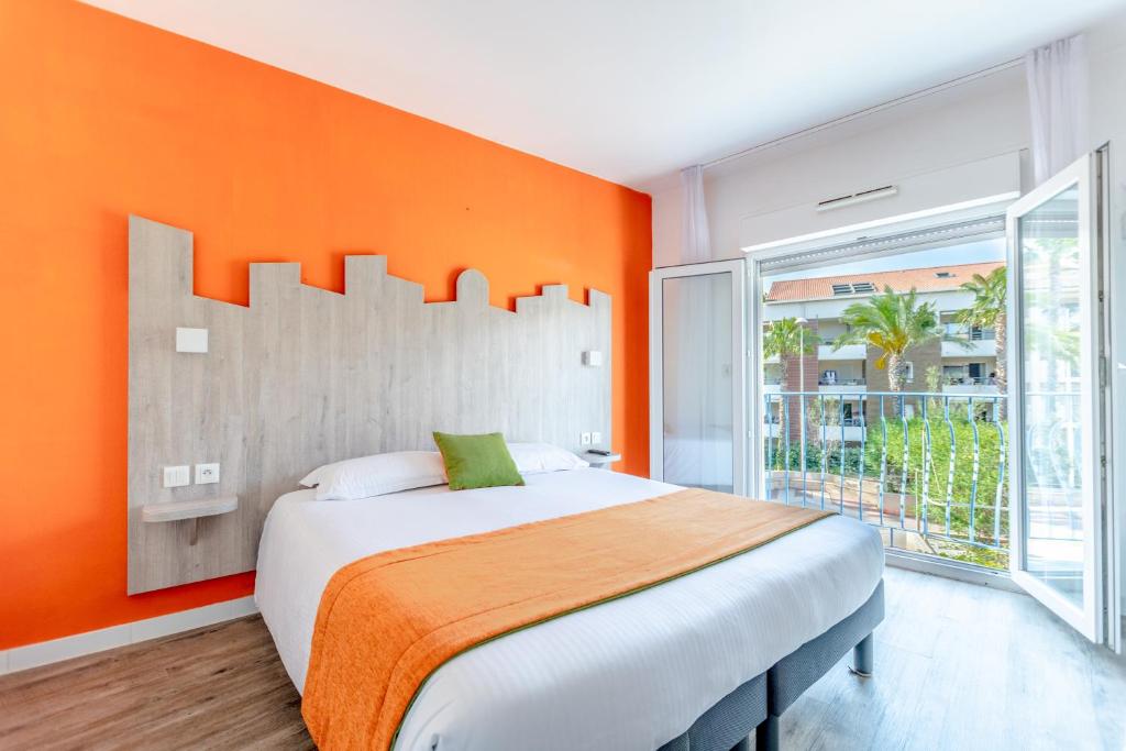 sypialnia z dużym łóżkiem z pomarańczową ścianą w obiekcie Hotel Provencal w miejscowości Saint-Raphaël