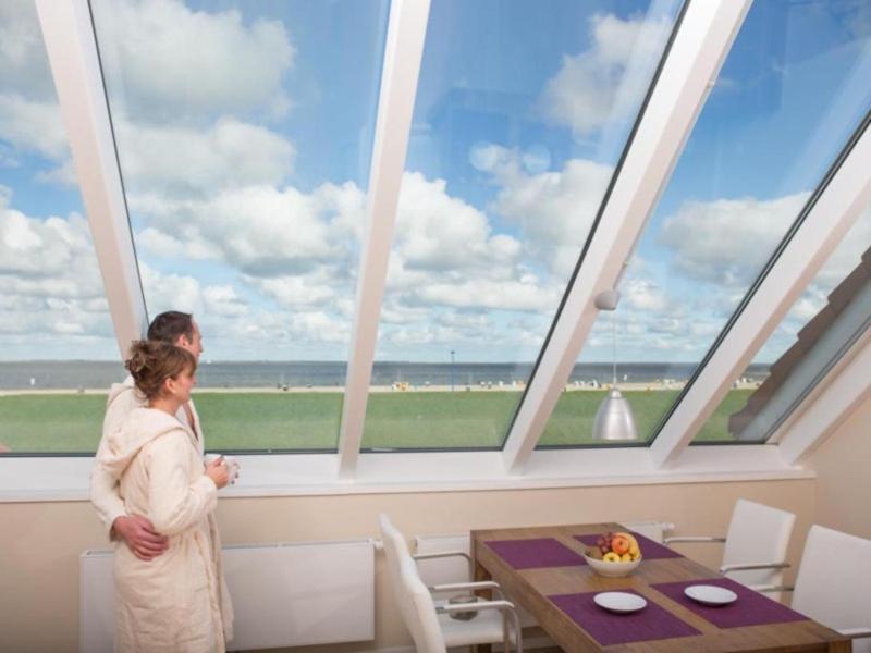 a man and woman standing in front of a large window at BadeWerk Appartements in Neuharlingersiel