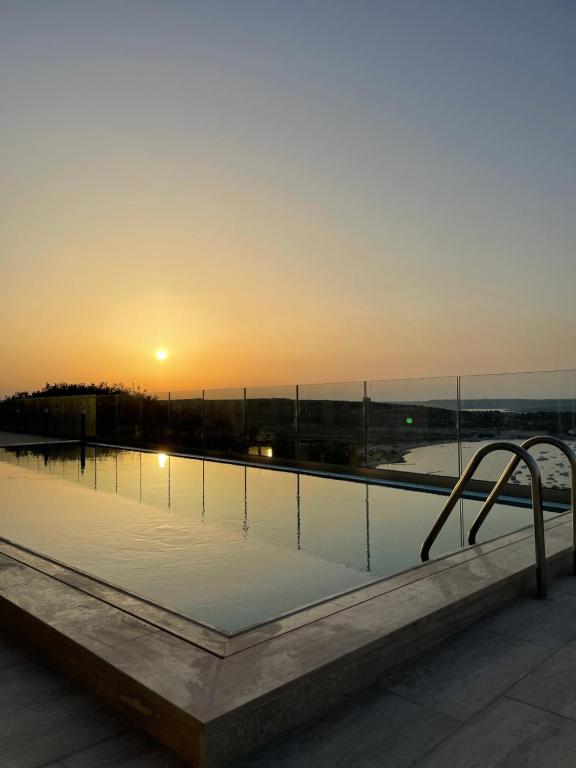 a swimming pool with the sunset in the background at Hotel VIU57 in Mellieħa