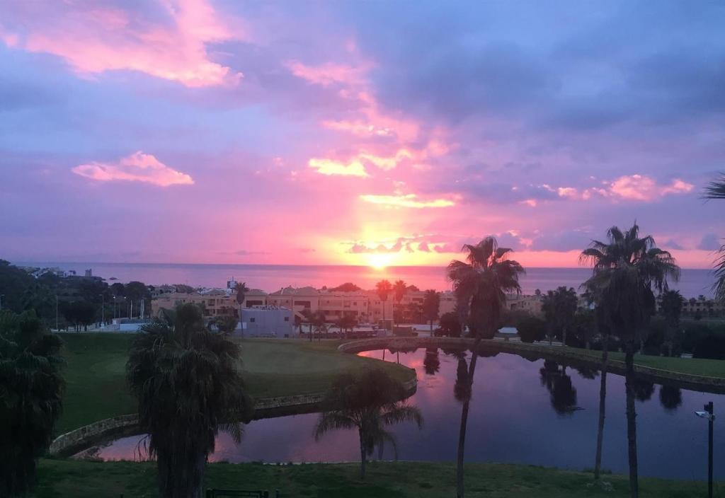 a sunset over a golf course with palm trees and a pond at El Patio de Doña Julia in Bahia de Casares