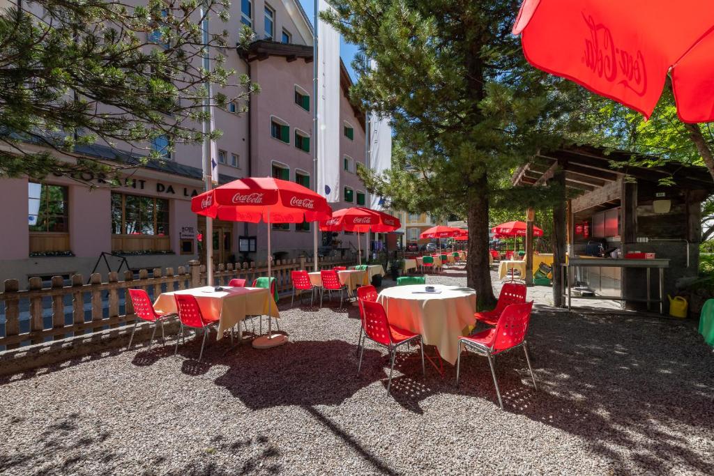 Hotel Post Sils Maria في سيلس ماريا: مجموعة طاولات وكراسي مع مظلات حمراء