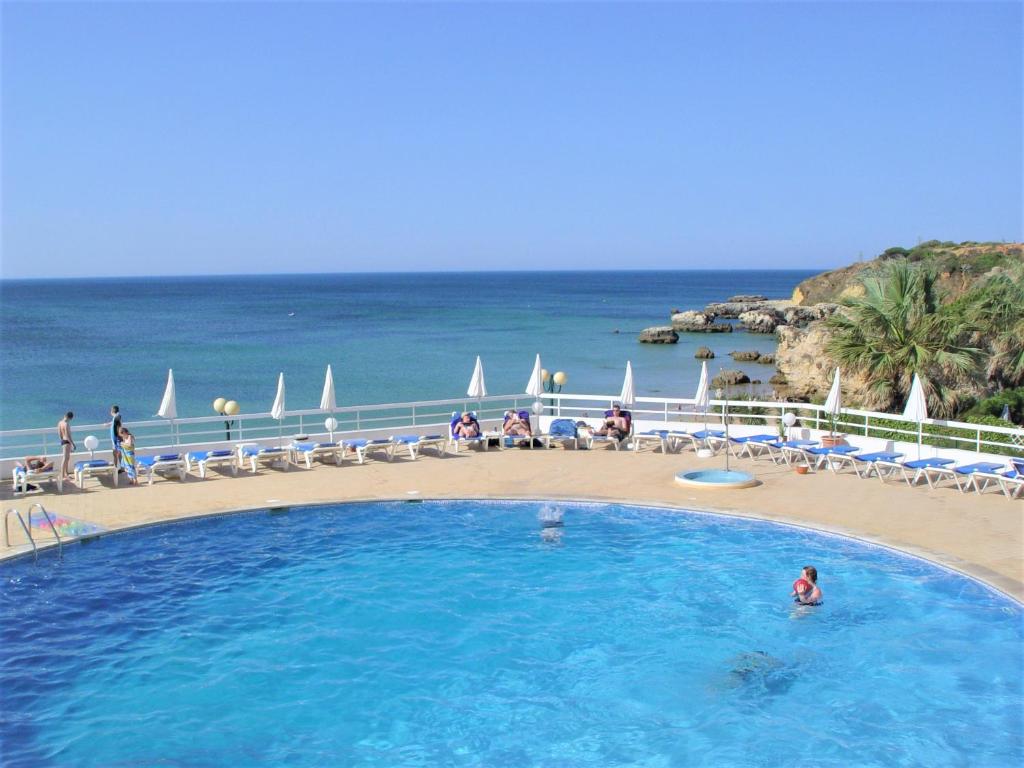 a large swimming pool with a beach and the ocean at Apartamentos Borda D´Agua in Albufeira