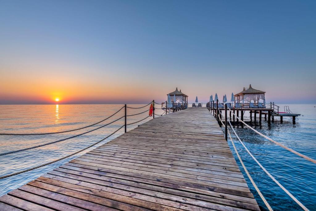 een houten pier in het water bij zonsondergang bij Amara Comfort Resort in Kemer
