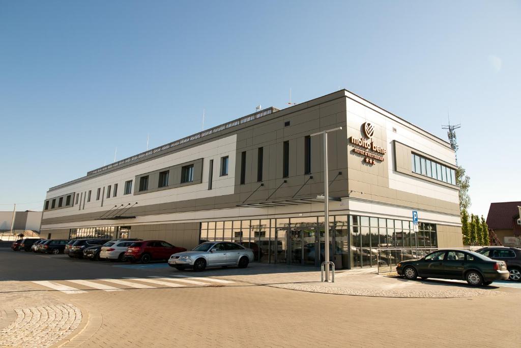 Molto Bene Hotel & Restaurant في Skórcz: مبنى كبير به سيارات تقف في موقف للسيارات