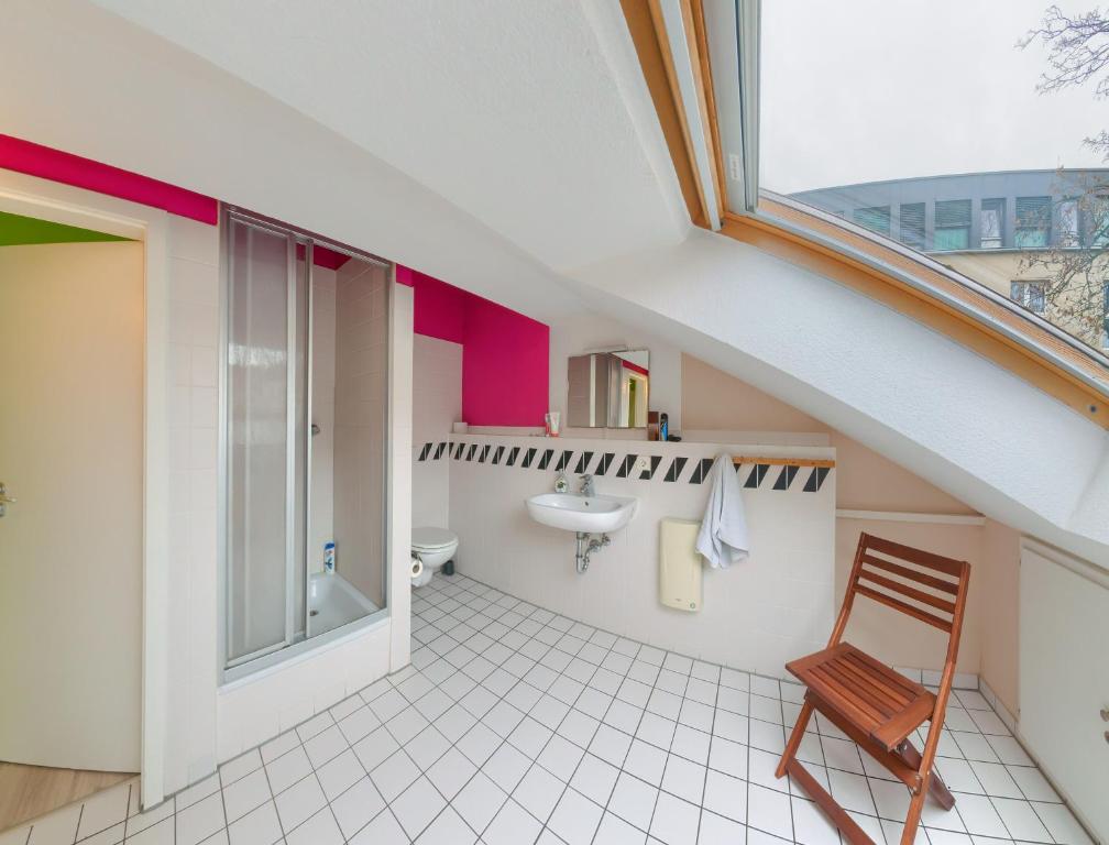 un bagno mansardato con lavandino e sedia di Labyrinth Hostel Weimar a Weimar