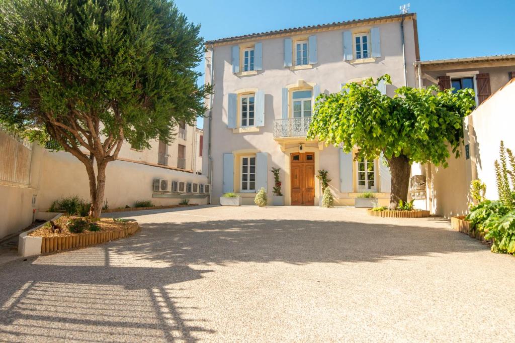 una grande casa bianca con alberi nel vialetto di La Maison des Vendangeurs en Ville a Narbonne