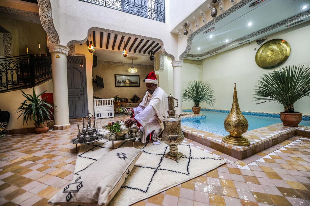 un hombre con un sombrero de Santa sentado en una habitación con piscina en Riad Milouda en Marrakech