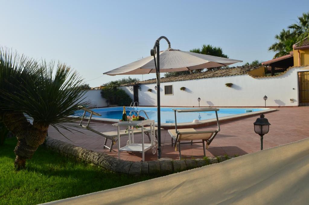 um pátio com uma mesa e um guarda-sol ao lado de uma piscina em Il Cigno Reale - White - Rooms Leasing tuoristic Ragusa em Chiaramonte Gulfi