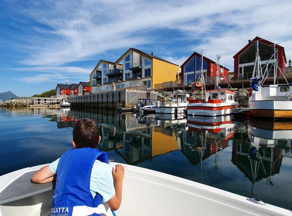 Um rapaz está sentado num barco na água. em Lofoten Seaside em Ballstad