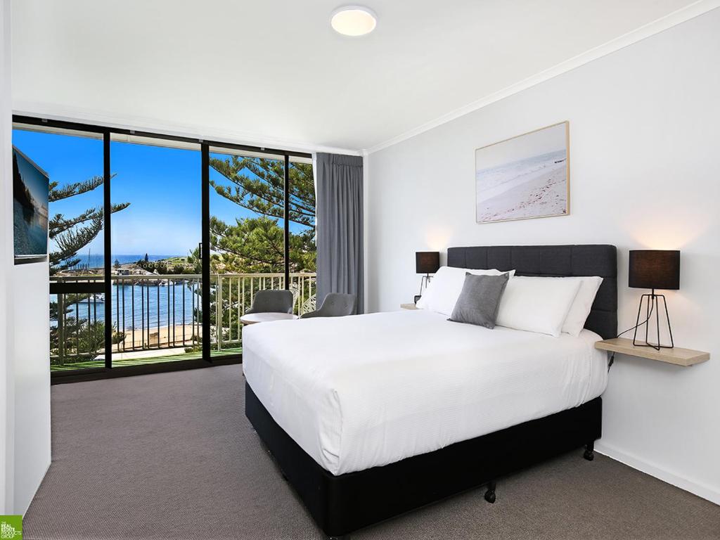 a bedroom with a large white bed and large windows at Boat Harbour Motel in Wollongong