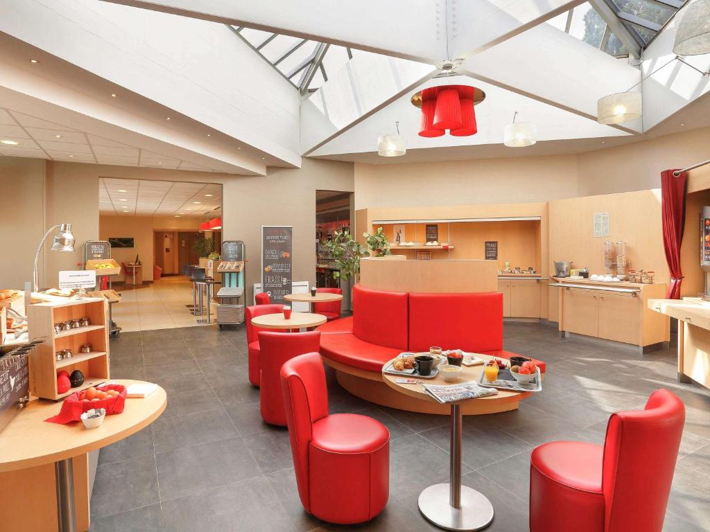 une cafétéria avec des chaises et des tables rouges ainsi qu'une cuisine dans l'établissement Ibis Le Havre Sud Harfleur, à Harfleur