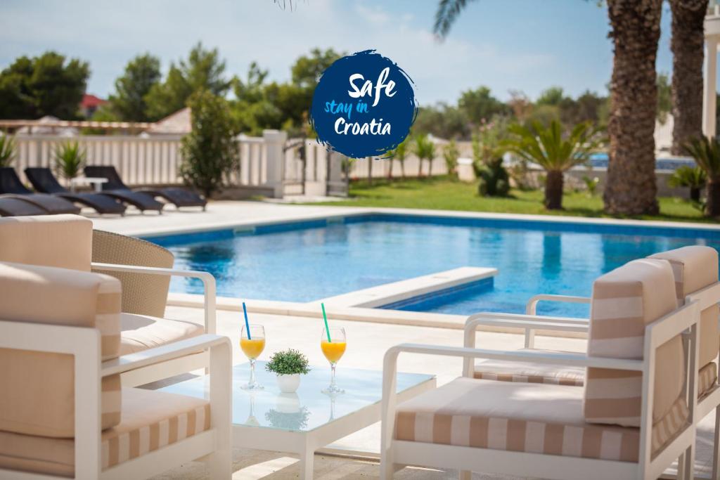 a pool with two glasses of orange juice on a table at Hotel Perla in Rogoznica