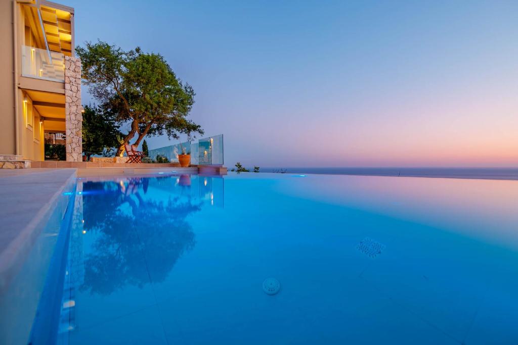 una piscina di fronte a un edificio con tramonto di Ocean View Luxury Villa Ethra a Città di Corfù