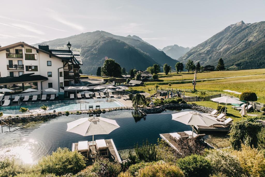 a resort with a pool with umbrellas and mountains at Hotel Schwaigerhof in Schladming