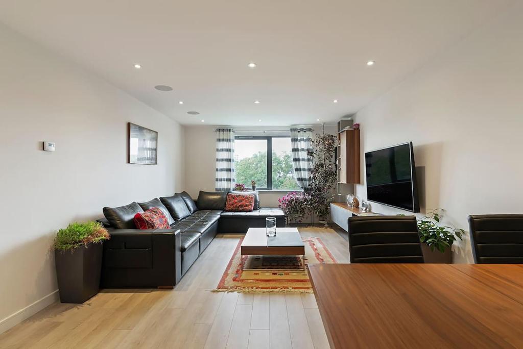 a living room with a black couch and a tv at 1-Bed Spacious Flat, North London, 15 Minutes to Central in New Southgate