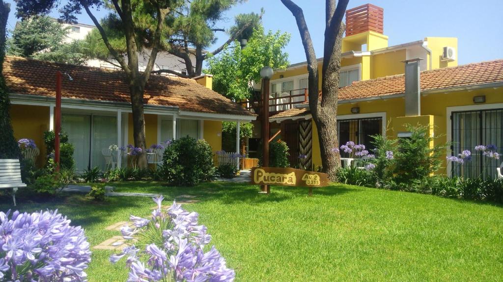 una casa amarilla con un patio con flores moradas en pucará en Villa Gesell