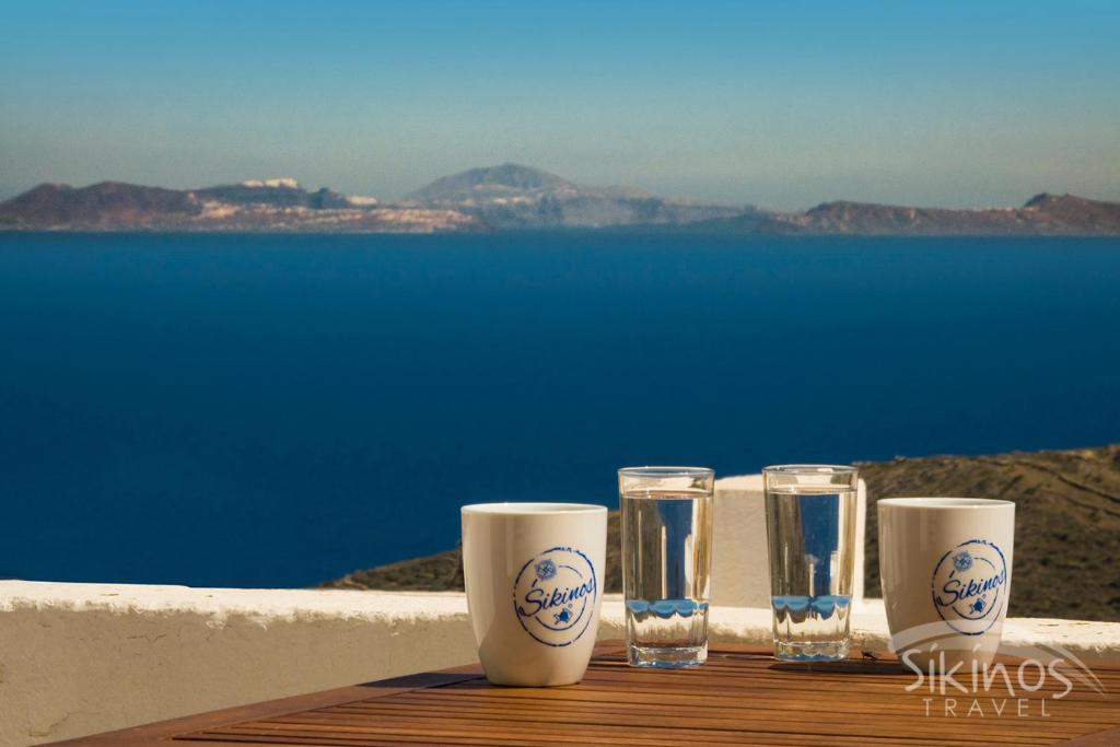 a table with four glasses and a view of the water at House Of Kastro in Sikinos