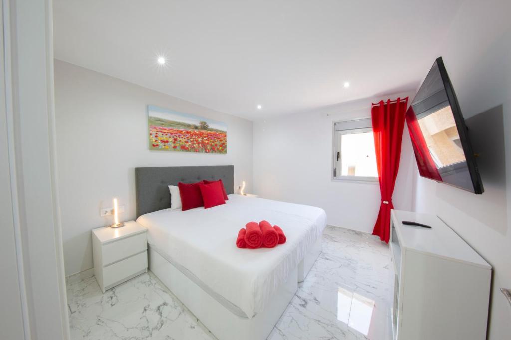 biała sypialnia z białym łóżkiem z czerwonymi poduszkami w obiekcie MEDANO4YOU The Austrian Holiday Home w mieście El Médano