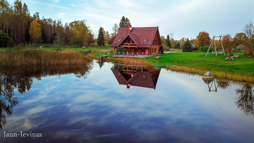une maison sur un lac avec sa réflexion dans l'eau dans l'établissement Jaun-Ieviņas, à Rauna