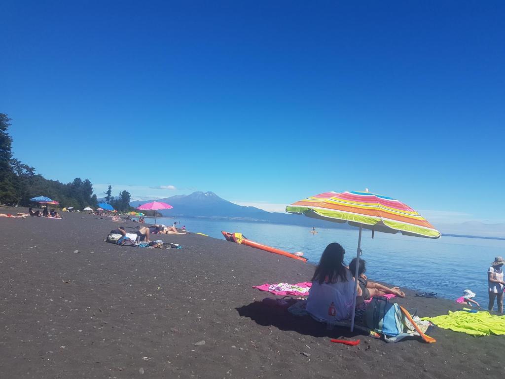 a group of people sitting on a beach with an umbrella at Lago Llanquihue Casa playa Ensenada in Puerto Clocker