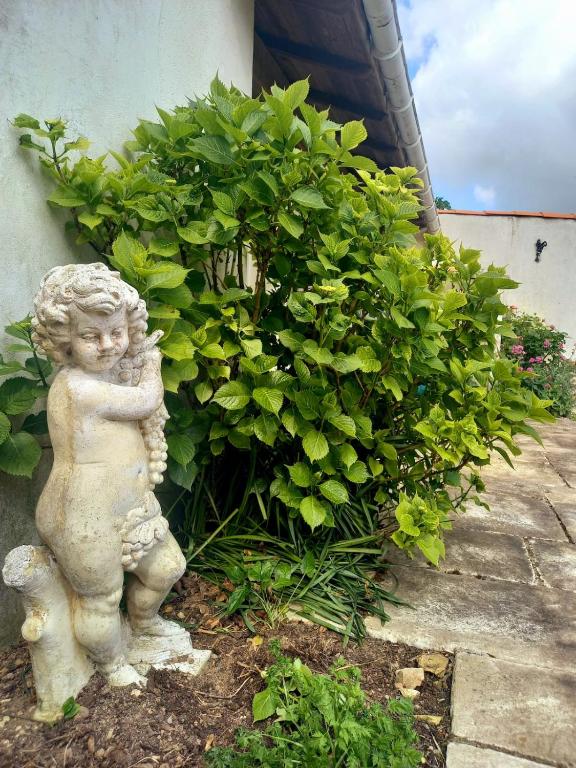 Une statue d'un petit ange debout à côté d'une brousse dans l'établissement Chez Chris, à Jard-sur-Mer