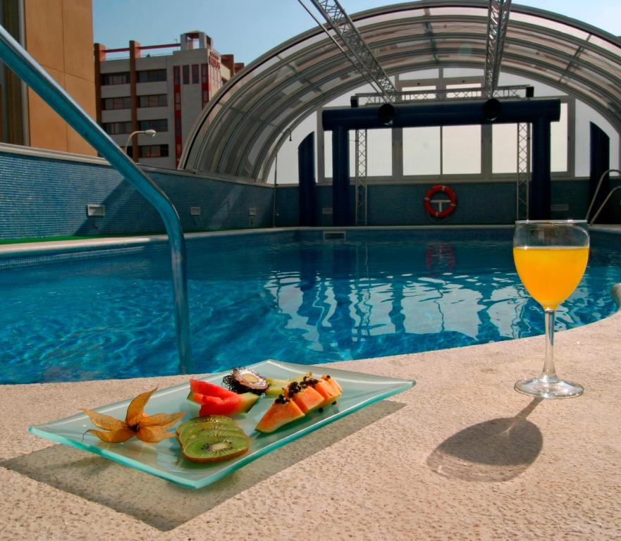a plate of food and a glass of wine next to a swimming pool at Vértice Sevilla in Seville