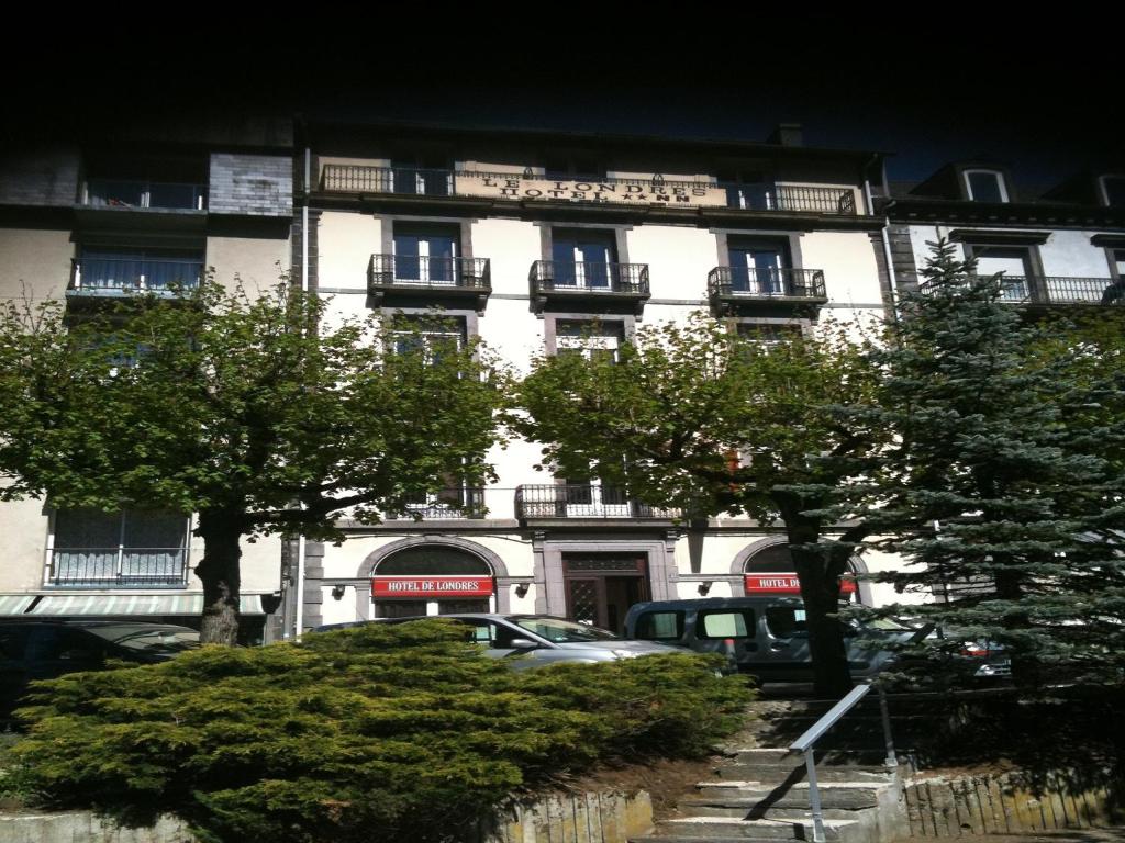 ein weißes Gebäude mit davor geparkt in der Unterkunft Hôtel de Londres in Le Mont-Dore