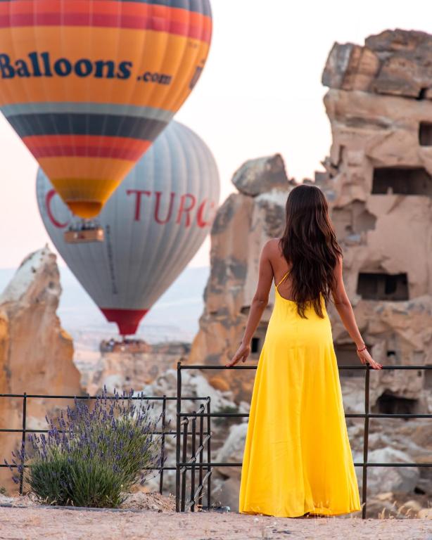 a woman in a yellow dress looking at hot air balloons at Seki Cave Hotel, Wake Up to Hot Air Balloons in Göreme