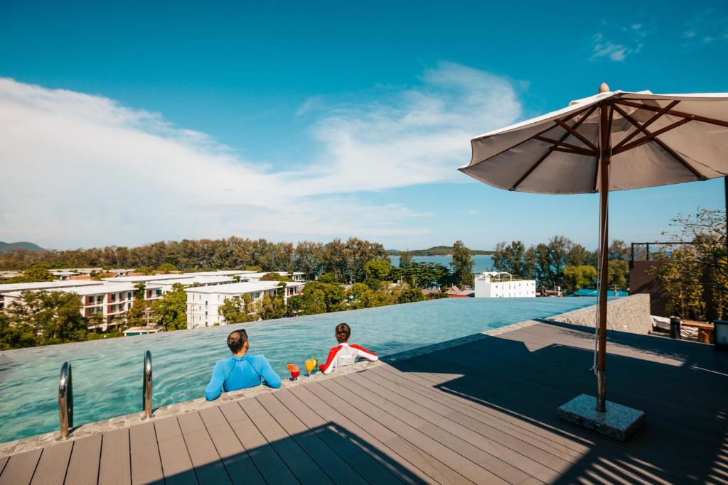 two people sitting on a dock next to the water at The Proud Rawai Resort in Rawai Beach