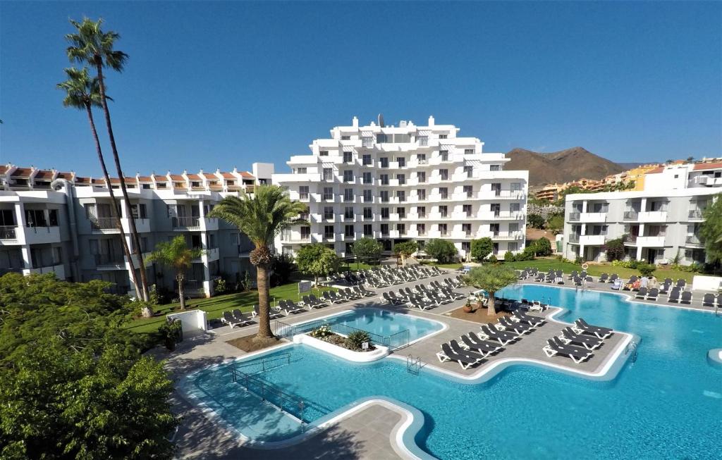 ein Hotel mit einem Pool und Stühlen sowie einem Gebäude in der Unterkunft HG Tenerife Sur in Los Cristianos