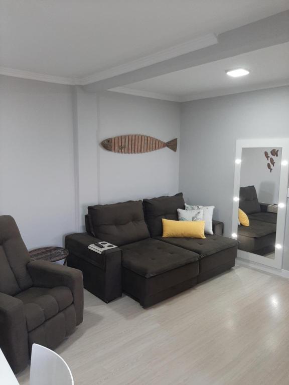 ein Wohnzimmer mit einem braunen Sofa und einem Spiegel in der Unterkunft Apartamento na Praia da Enseada, 100 mt praia in São Francisco do Sul