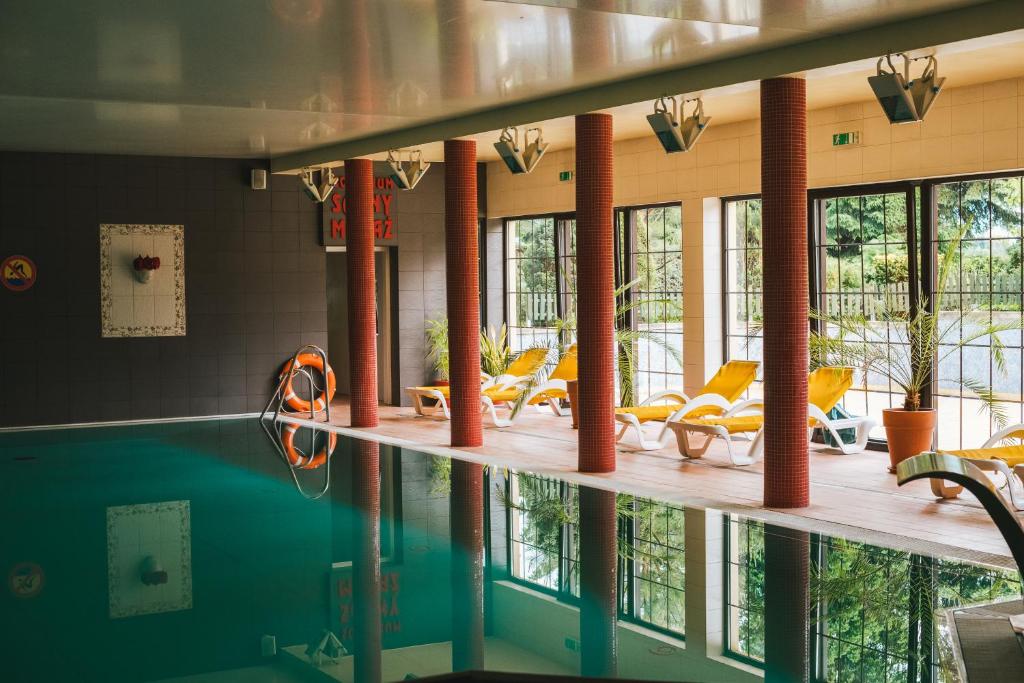 a swimming pool with yellow chairs and tables and windows at Hotel Chata Za Wsią in Mysłakowice