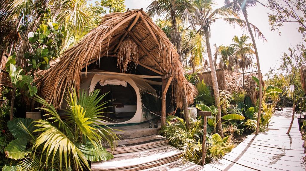una cabaña con techo de paja en un jardín en Uman Glamping & Cenote Tulum, en Tulum