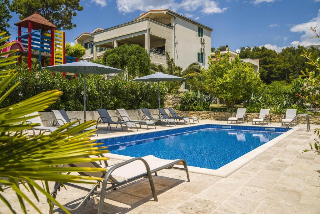 a pool with chairs and umbrellas next to a house at Villa Dvori Viškovi in Podstrana