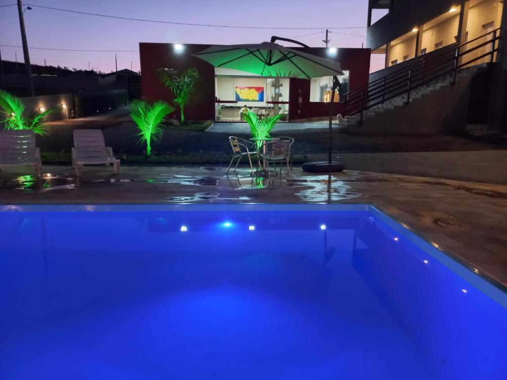 a swimming pool at night with a green umbrella at Pousada Morada dos Pássaros in Capitólio