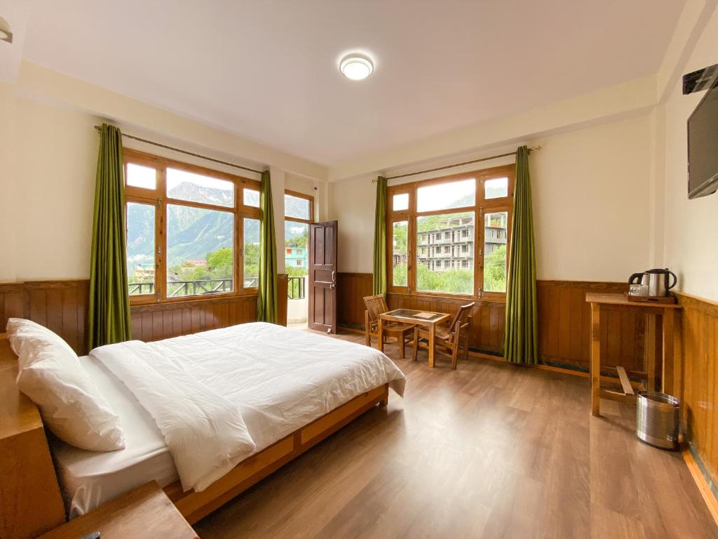 a bedroom with a bed and a table and windows at Hotel KALPA in Kalpa