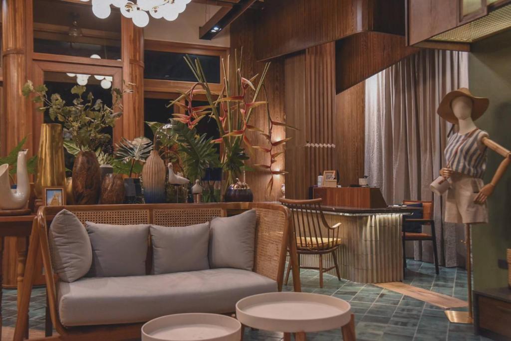 A richly styled lounge with a rattan sofa, indoor plants, and a mannequin display.
