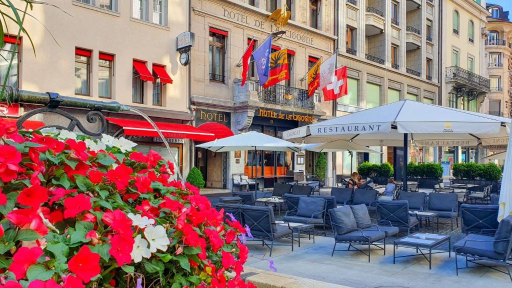 un patio con mesas, sillas y flores rojas en Hôtel de la Cigogne, en Ginebra