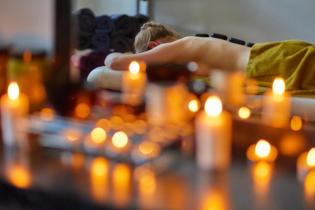 Person receiving hot stone massage on a spa table, candles blurred in foreground, tranquil mood.