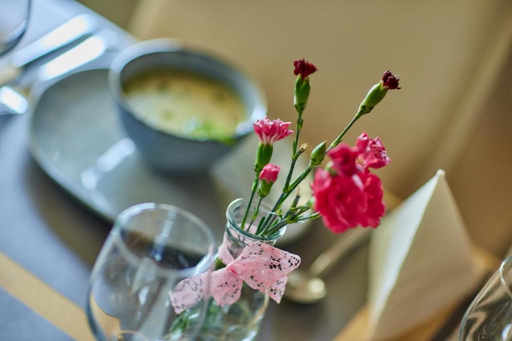 Small glass vase holding pink carnations tied with lace ribbon on a dining table, softly blurred background.