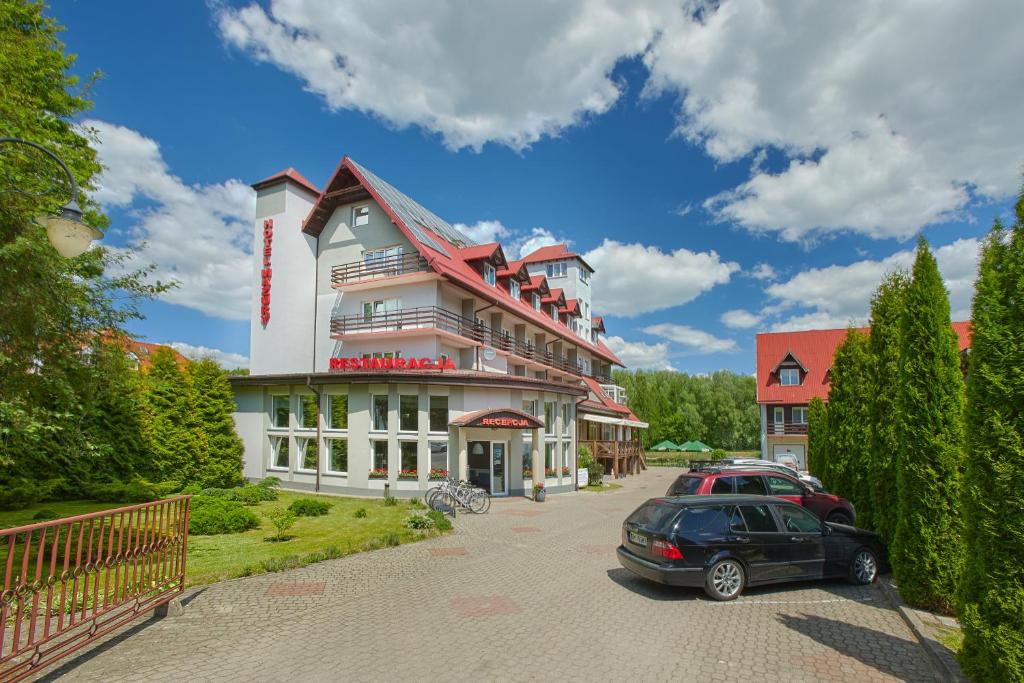 Large multi-story hotel with red roofs and balconies, parking lot and green landscaping under blue sky.