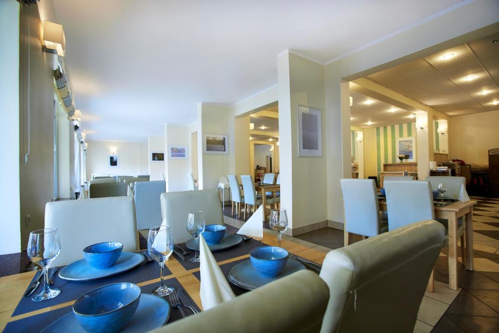 Light-filled restaurant dining room with neatly set table, blue bowls, wine glasses, and white chairs.
