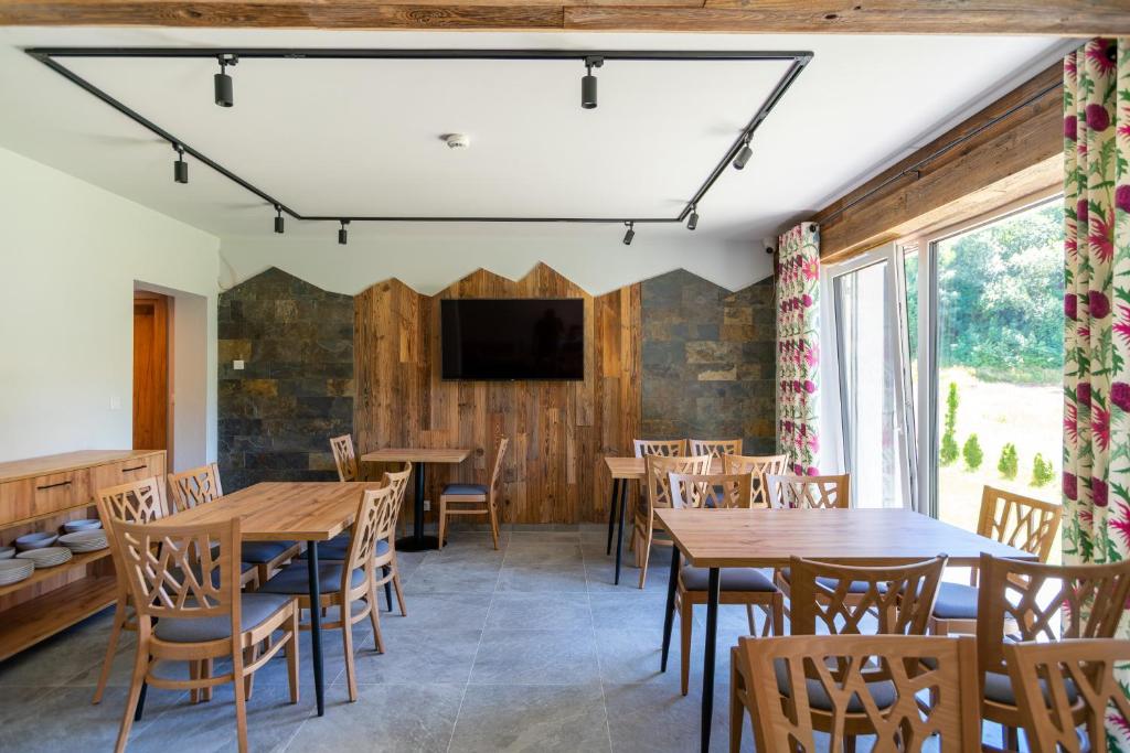 Communal dining room with wooden tables and chairs, TV on wood-accent wall, large windows with floral curtains.