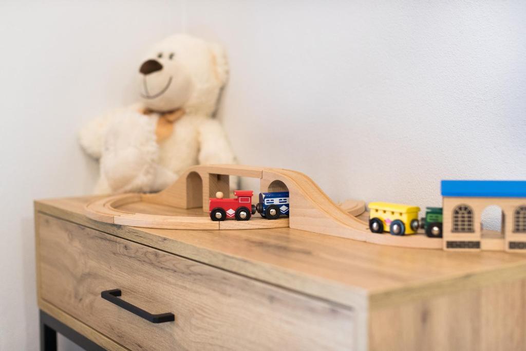 Wooden toy train set on dresser with blurred teddy bear in cozy child's corner.
