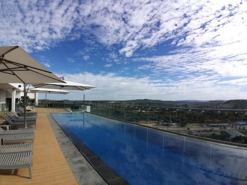 a swimming pool with chairs and an umbrella at Menlyn Maine Apartments in Pretoria