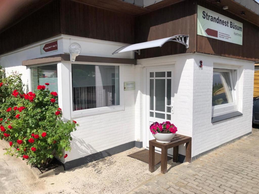 un pequeño edificio blanco con flores rojas y una mesa en Strandnest Büsum Apartments, en Büsum
