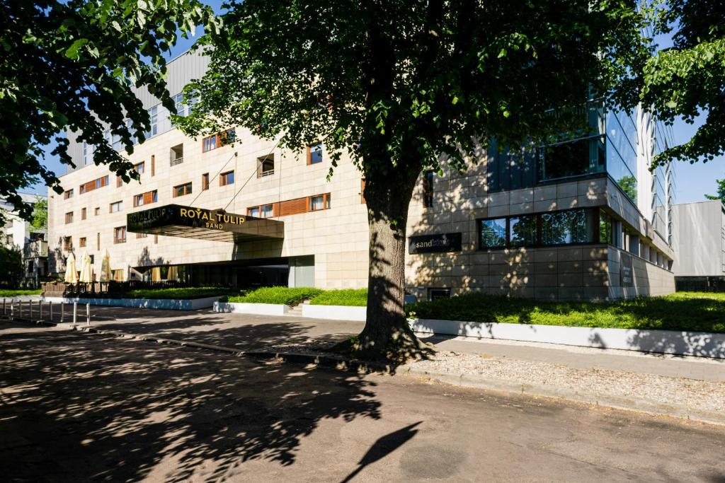 un edificio con un árbol delante de él en Royal Tulip Sand Kolobrzeg, en Kołobrzeg