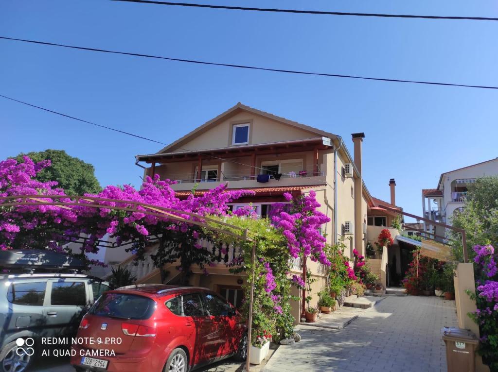 een rode auto geparkeerd voor een gebouw met paarse bloemen bij Apartments Iva in Pakoštane