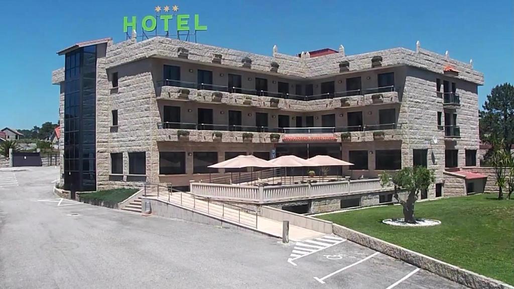 ein Hotel mit einem großen Gebäude mit Tischen und Sonnenschirmen in der Unterkunft Hotel Pedramar in A Lanzada